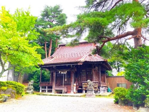 Small traditional wooden shrine with a red-tiled roof nestled in a green garden, with stone lanterns nearby.